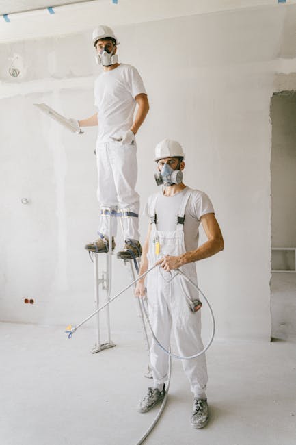 Two painters in protective gear working on a home renovation project, wearing masks and white uniforms.