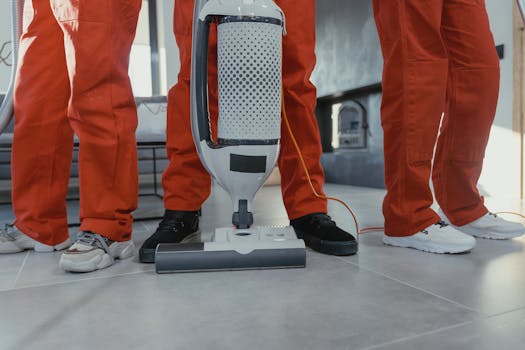 Team of professional cleaners in red uniforms using a vacuum cleaner indoors.