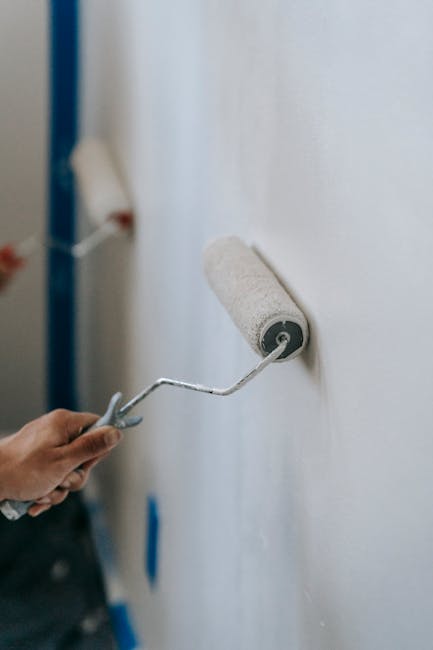 Close-up of hands using paint rollers to renovate an interior wall of a home.